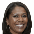 Alexis Edwards, with straight dark hair, hoop earrings, and a wide smile, poses in front of a white background.