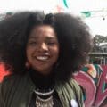 Angie Thomas with natural curly hair smiles outdoors before colorful graffiti and festive flags, evoking scenes from her novels.